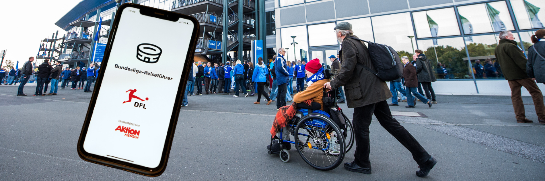 • Ein Fan im Rollstuhl und eine Begleitperson im Umlauf eines Stadions. Davor ein Handy mit dem Startbildschirm der App mit Bundesliga-Reiseführer-Schriftzug und den Logos von DFL und Aktion Mensch.